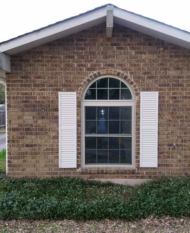 New white arched replacement window with shutters on a brick home