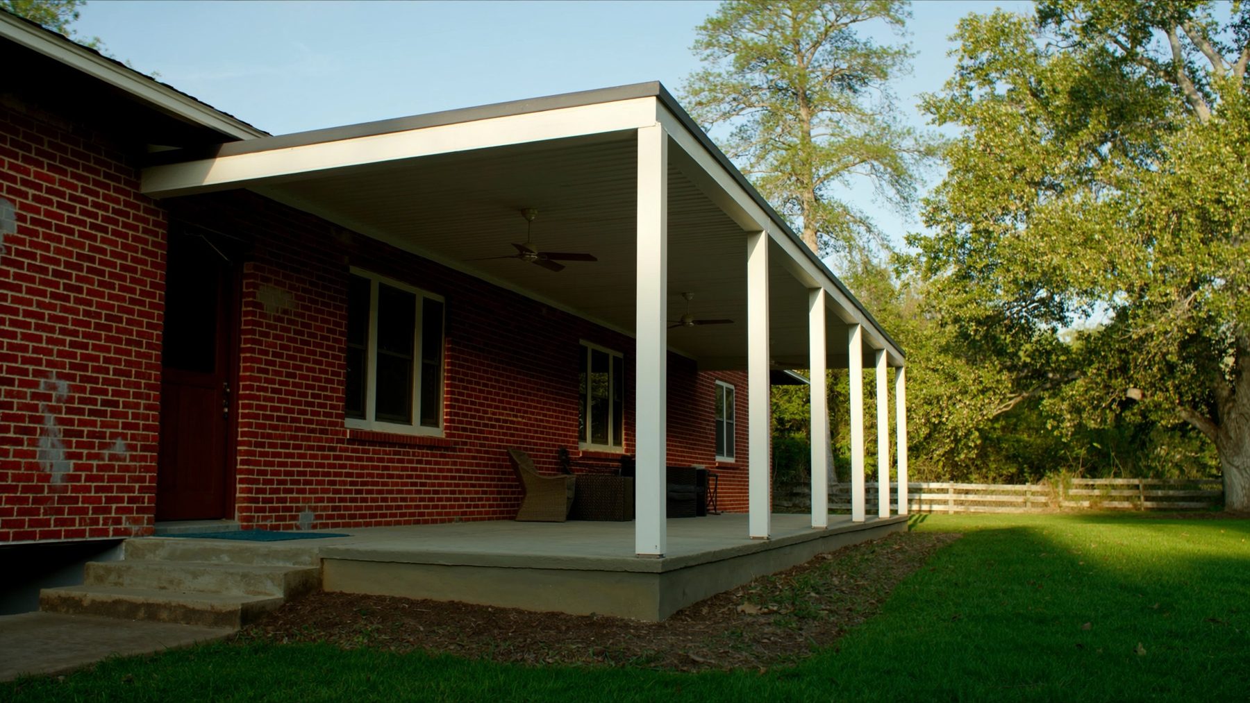 White insulated patio cover on a red brick ranch home in the afternoon sun
